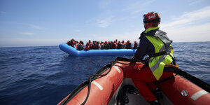 Eine Person mit gelber Weste sitzt auf einem Schlauchboot, das Kurs nimmt auf ein Flüchtlingsboot