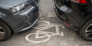Ein Fahrradweg ist von zwei Autos zugeparkt