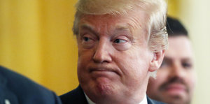 Trump mit zusammengepressten Lippen vor gelbem Hintergrund