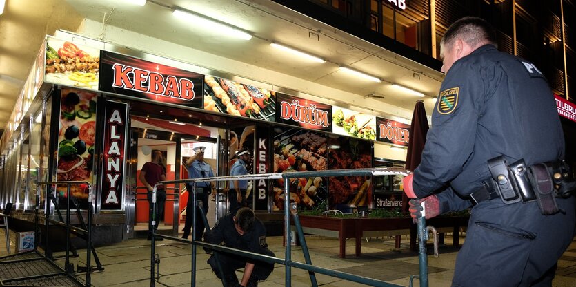 Polizisten stellen Absperrgitter vor den erleuchteten Döner-Imbiss