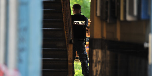 Ein Polizist steht in einem dunklen Hauseingang, das Gesicht der geöffneten Tür zugewandt