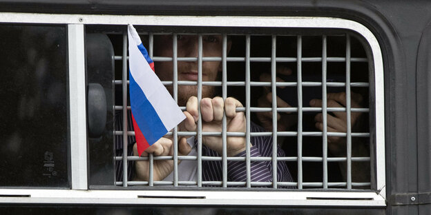 Ein festgenommener Demonstrant schwenkt aus einem Polizeiwagen heraus eine russische Fahne