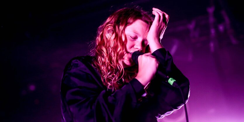 Kate Tempest singt mit geschlossenen Augen und Hand auf der Stirn