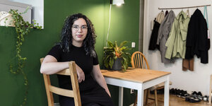 Eine dunkelhaarige Frau sitzt an einem Küchentisch vor einer grünen Wand