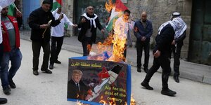 Eine Gruppe von Männern mit palästinensischen Flaggen protestiert auf einer Straße. In ihrer Mitte ist ein Plakat aufgerichtet auf dem "No for the deal of the century" steht. Es steht in Flammen