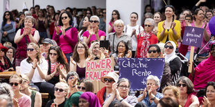 Frauen sitzen und stehen mit Transparenten auf einem Platz