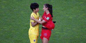 Eine Spielerin des US-Teams im roten Trikot spricht auf dem Rasen mit einer Spielerin aus dem Thailändischen Team in gelbem Trikot