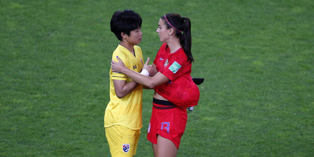 Eine Spielerin des US-Teams im roten Trikot spricht auf dem Rasen mit einer Spielerin aus dem Thailändischen Team in gelbem Trikot