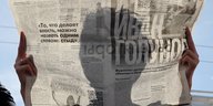 Eine Person hält auf einer Demo eine russische Zeitung vor ihr Gesicht