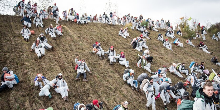 Demonstranten in weißen Maleranzügen rutschen eine Berg runter