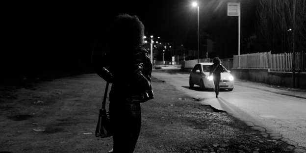 Frauen stehen im Dunkeln am Straßenrand, ein Auto hält.