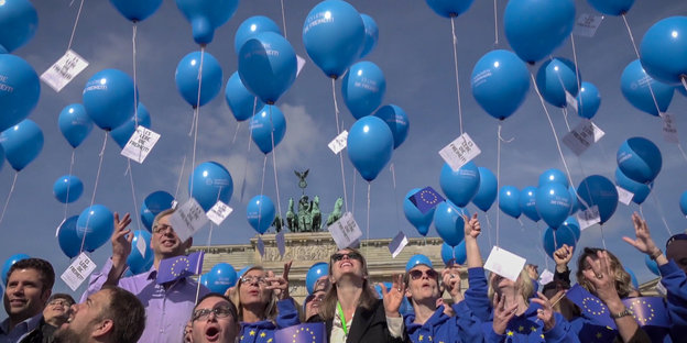 Menschen vor dem Brandenburger Tor lassen blaue Luftballons in die Luft steigen