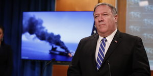 US-Außenminister Mike Pompeo steht bei einer Pressekonferenz vor einem Fernsehbildschirm auf dem ein brennender Öltanker zu sehen ist