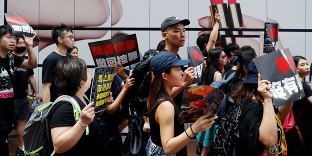 Demonstranten in schwarzen Oberteilen halten Schilder in die Höhe