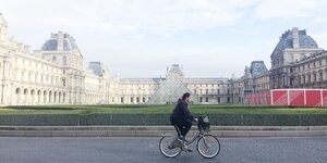 Ein Fahrradfahrer fährt am Louvre in Paris vorbei