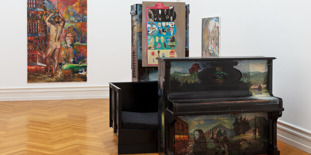 Ein bemaltes Klavier in einem Ausstellungsraum, dahinter Gemälde und Eisreklame