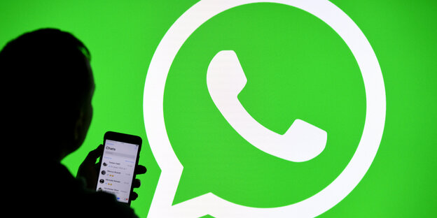 Schattenriss eines menschen mit Smartphone vor dem grünen WhatsApp-Logo
