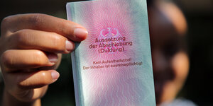 Eine junge Frau aus Afrika hält einen Ausweis für Flüchtlinge in der Hand mit dem Titel: Aussetzung der Abschiebung (Duldung)