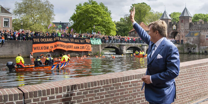 Mann im Anzug winkt Demonstranten am Wasser zu