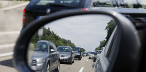 Im Rückspiegel eines Wagens sieht man auf der Autobahn fahrende Autos.