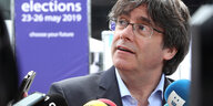 Carles Puigdemont sitzt vor Mikrophonen, hinter ihm ein Banner der Europawahl.