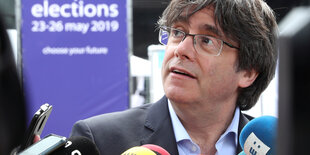 Carles Puigdemont sitzt vor Mikrophonen, hinter ihm ein Banner der Europawahl.