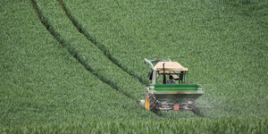 Ein Traktor fährt ein grünes Feld entlang und hinterlässt tiefe Spuren.