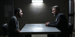 Zwei Männer sitzen sich im Dunkeln an einem Veröhrtisch gegenüber