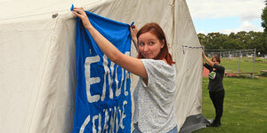 Zwei junge Frauen hängen Transparente an ein weißes Zelt