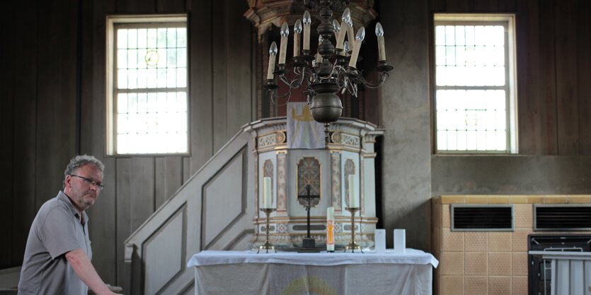 Ein Mann, der Pfarrer ist, steht in einer Kirche links neben dem Altar.