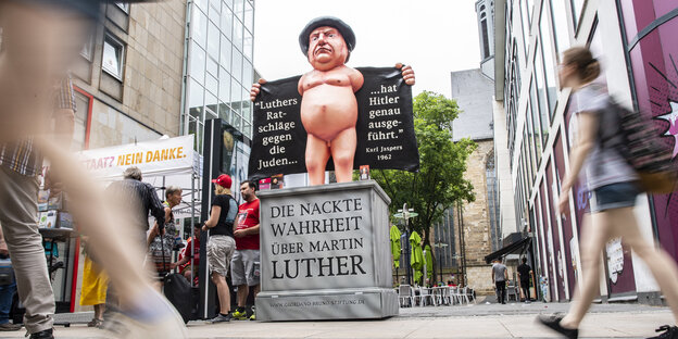 or Beginn des 37. Deutschen Evangelischen Kirchentages gehen Passanten in der Dortmunder Fußgängerzone an einer Luther symbolisierenden Pappfigur vorbei, auf der „Luthers Ratschläge gegen die Juden hat Hitler genau ausgeführt“ steht