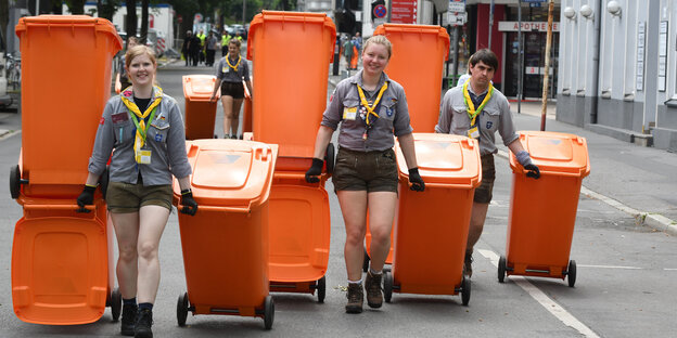 Pfadfinder ziehen orange Mülltonnen hinter sich her
