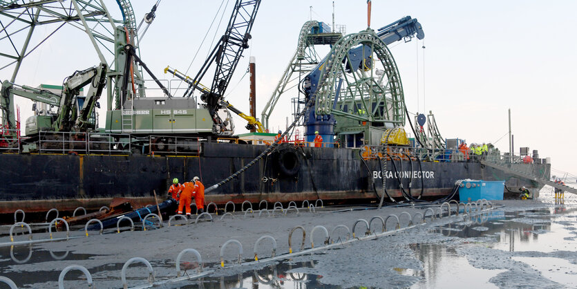 Das Endstück eines 516 Kilometer langen Seekabels wird von dem Kabelverlegeschiff "Boka Connector" im Watt unter dem Deich hindurch an Land gezogen.