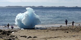 Kinder spielen neben einem Eisblock am Strand in Grönland