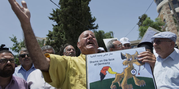 Ein Mann protestiert mit einem Schild auf dem "Shame on the face of Germany" steht