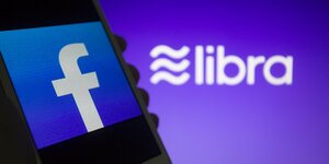 Ein Smartphone mit Facebooksymbol, dahinter das Libra-Symbol