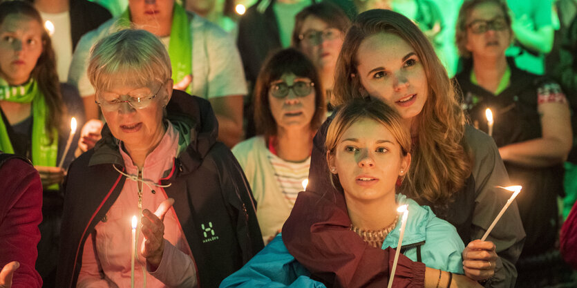 Mehrere Frauen halten Kerzen und umarmen sich