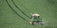 Ein Bauer fährt mit einem Traktor über ein grünes Feld und zieht einen Düngestreuer hinter sich her