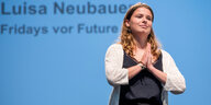 Eine junge Frau steht vor einem blauen Hintergrund und macht eine dankende Geste