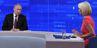 Wladimir Putin sitzt in einem blauen Fernsehstudio einer Moderatorin gegenüber