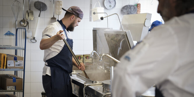 Koch Sebas­tian Drews mit Zweihand-Schneebesen an der Bratwanne