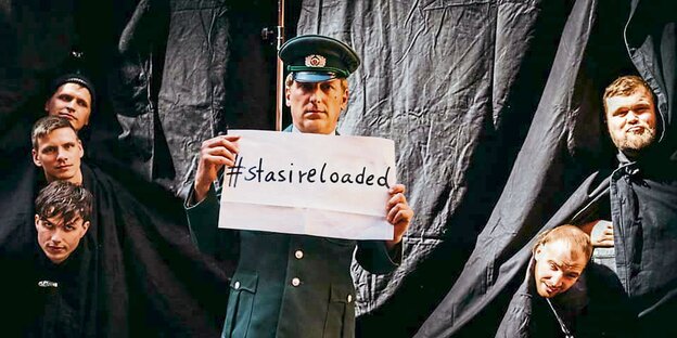 Ein Mann in Uniform trägt ein Schild mit der Aufschrift "#stasireloaded".
