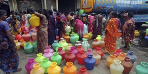 Eine Gruppe indischer Frauen füllt bunte Behälter bei einem Tanker mit Wasser.