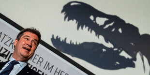 Markus Söder neben dem Schatten eines Dinosauriers