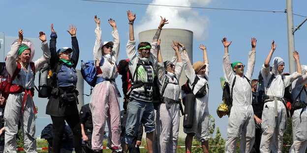 Menschen stehen mit erhobenen Händen auf einer Bahnstrecke nebeneinander, im Hintergrund ein Kühlturm