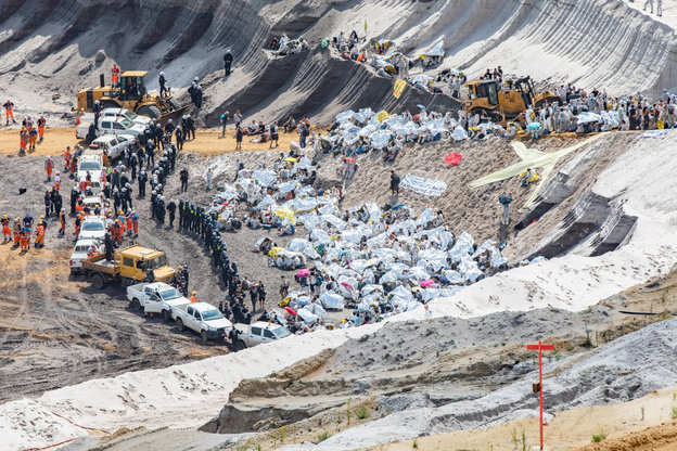 Die besetzte Grube von oben, Aktivisten in weiß, umzingelt von Polizisten und Fahrzeugen