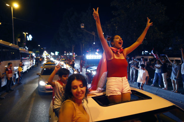 Eine junge Frau steht jubelnd auf einem Auto und macht mit beiden Händen das Victory-Zeichen
