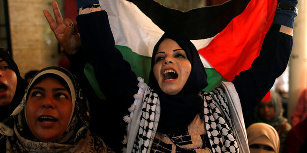 zwei Demonstrantinnen, eine hält eine Palästina-Flagge in die Höhe