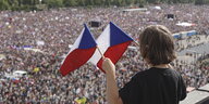 Tausende Menschen auf einem Platz, auf sie hinunter guckt ein kleiner Junge mit zwei Tschechien-Fahnen