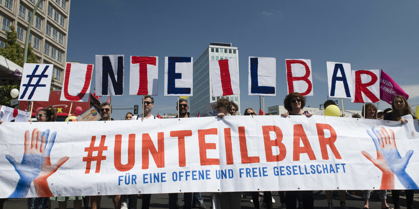 Mitglieder des Bündnisses "Unteilbar" stehen mit einem Transparent bei einer Demonstration